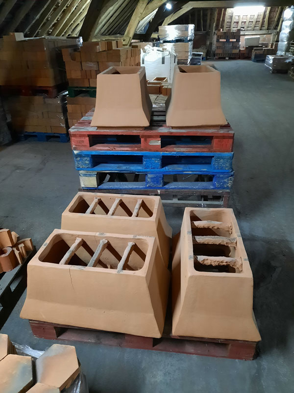 Mitres de cheminée en terre cuite crue rangées sur palettes à l'atelier.
